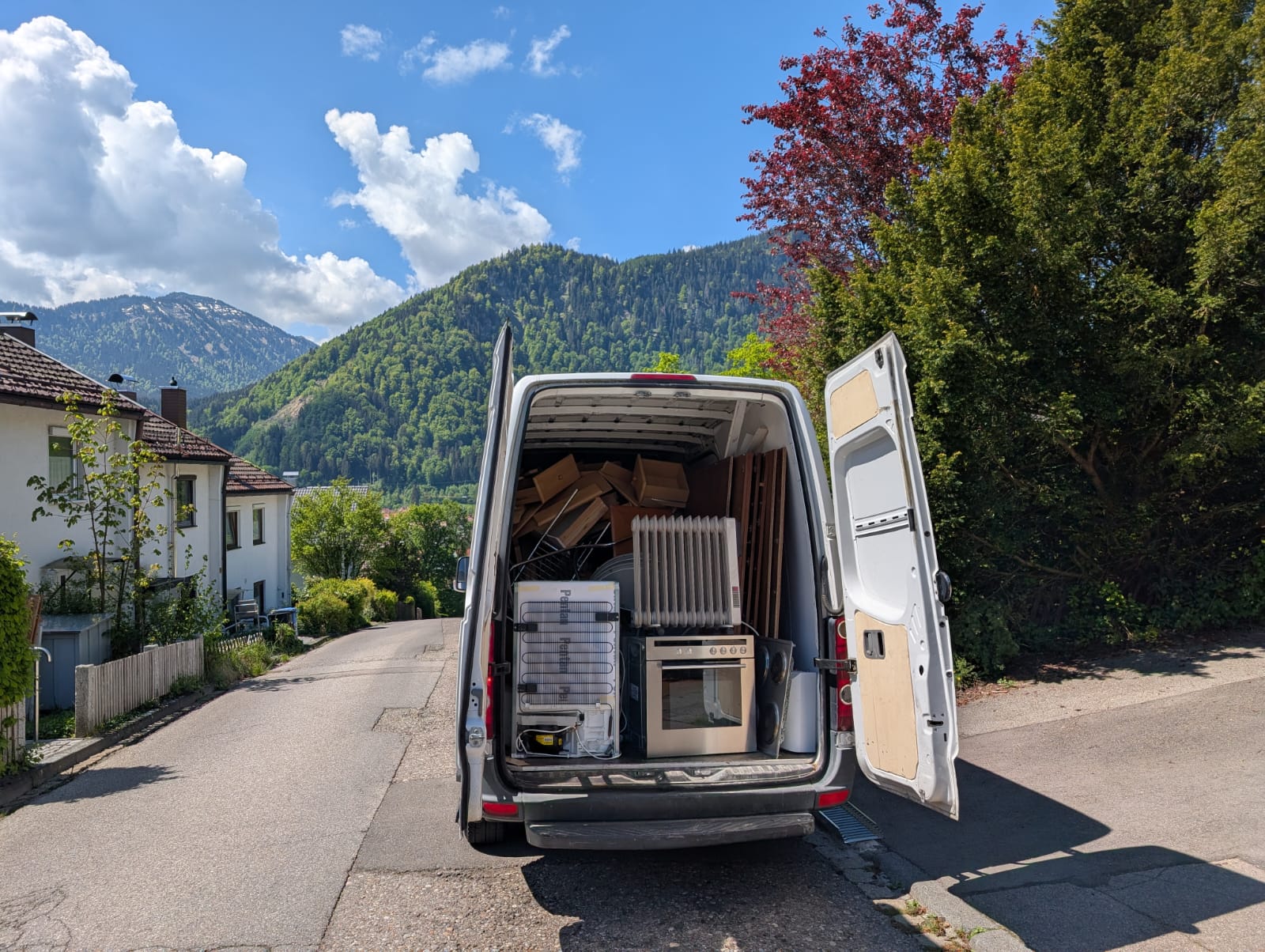Vollbeladenes Räumfahrzeug mit Möbeln und Elektrogeräten vor Allgäuer Bergkulisse